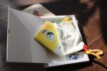 Geöffnetes ZeitFach mit Lätzchen und Kuscheltuch neben dem Baby-Fotobuch