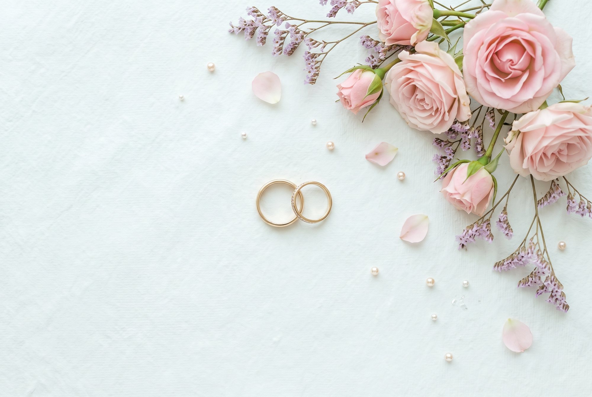 Zwei goldene Eheringe mit rosa Rosen und Perlen auf hellem Papier